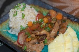 Plate with a pile of brown rice, stir-fry veggies, and sliced ​​pineapples