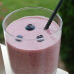 A PB&J smoothie with three blueberries and a black straw.