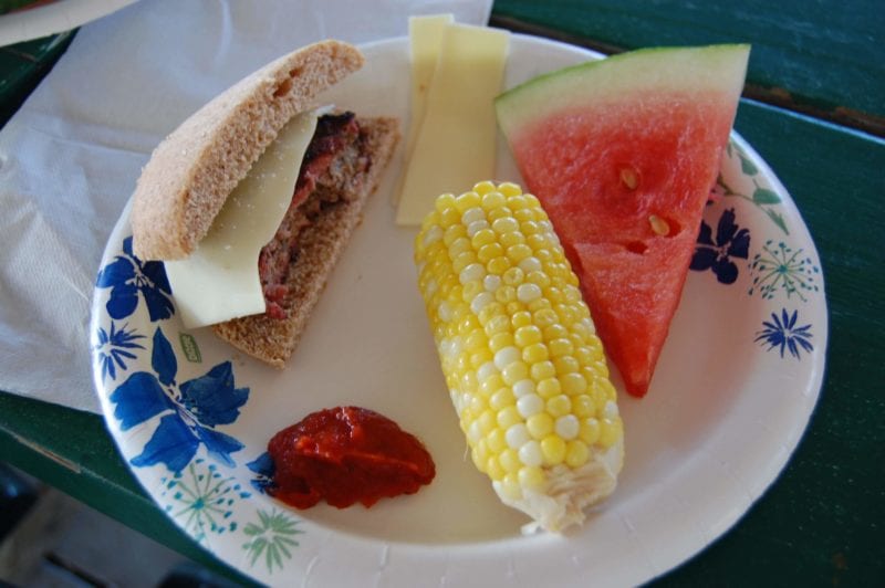 Hamburger, ear of corn, and a slice of watermelon on a plate. 