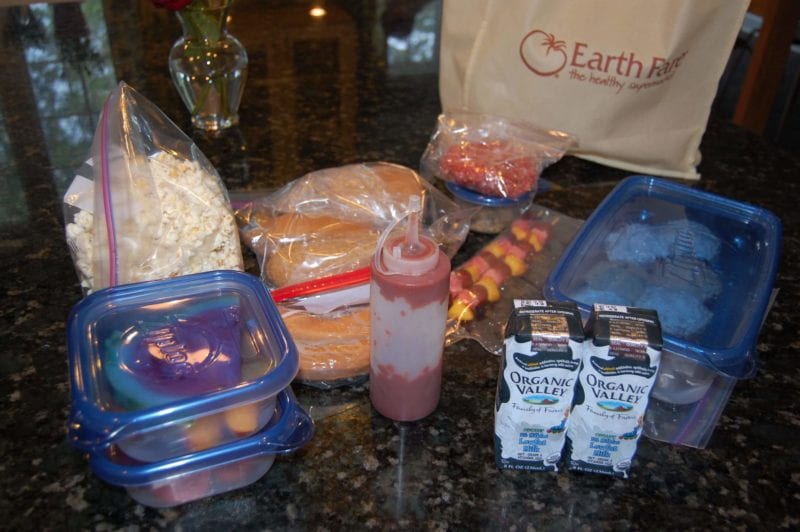 Prepared homemade food including ketchup, fruit, popcorn, and hot dogs. 