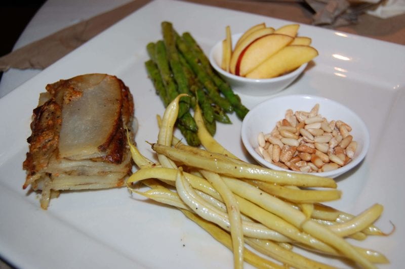 Peaches and toasted pine nuts, green beans, asparagus, and potato gratin on a plate. 
