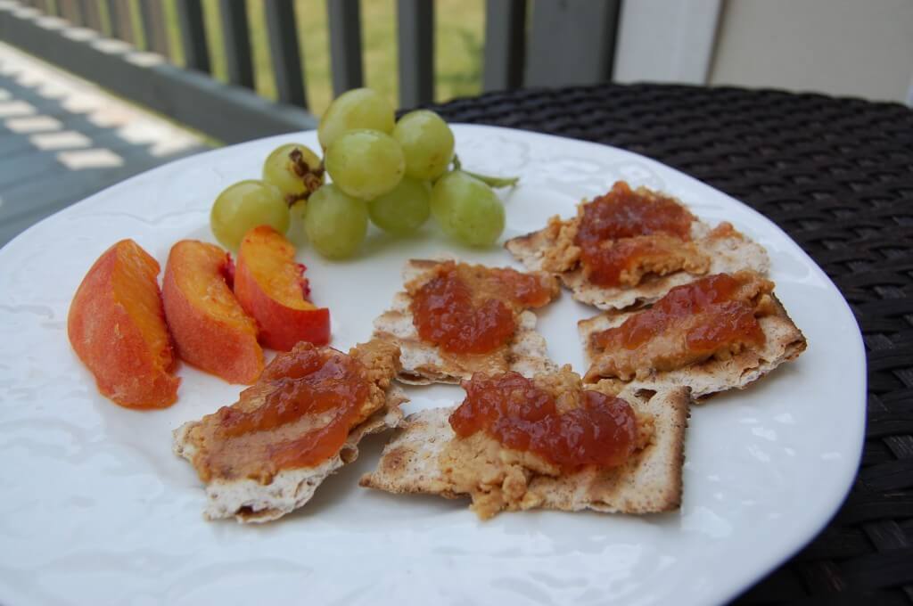 Matzo crackers with peanut butter and jelly on top with a side of peaches and grapes. 