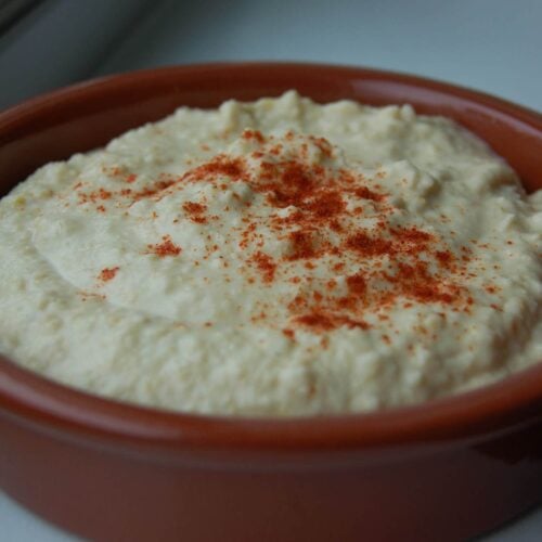 Homemade hummus in a brown bowl sprinkled with paprika.