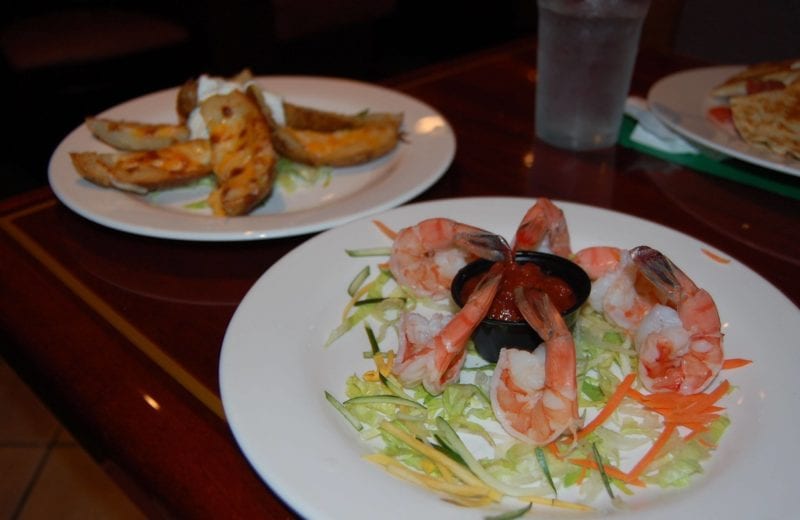 Shrimp cocktail over a bed of shredded veggies and a plate of potato skins. 