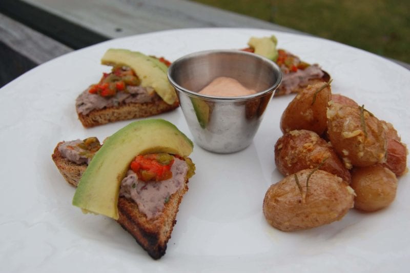 Open-faced sandwich with black bean hummus, bell  peppers, and avocado with a side of roasted potatoes and mango. 