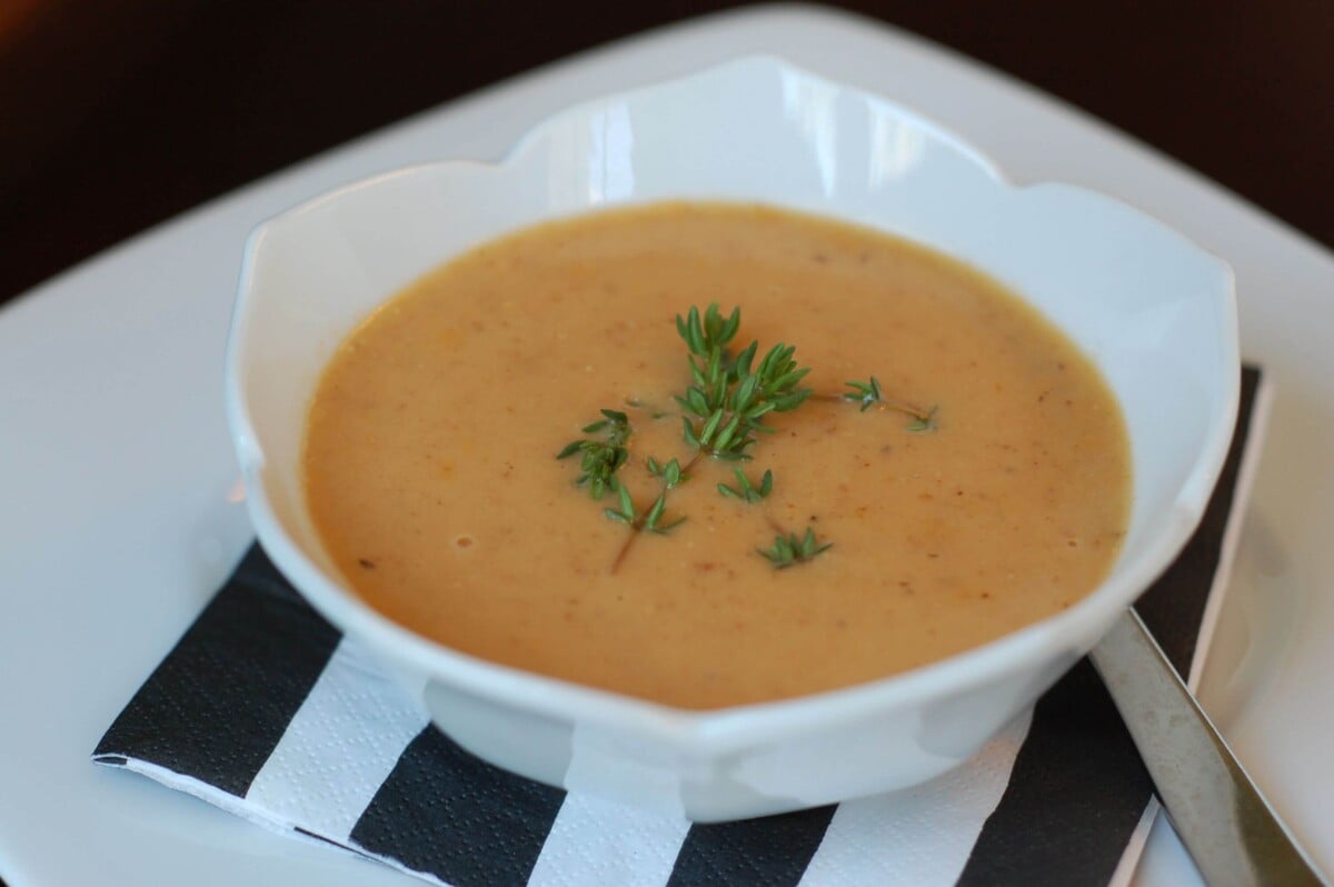 White bowl filled with warm, homemade, tomato bisque with a few sprigs of thyme on top. 