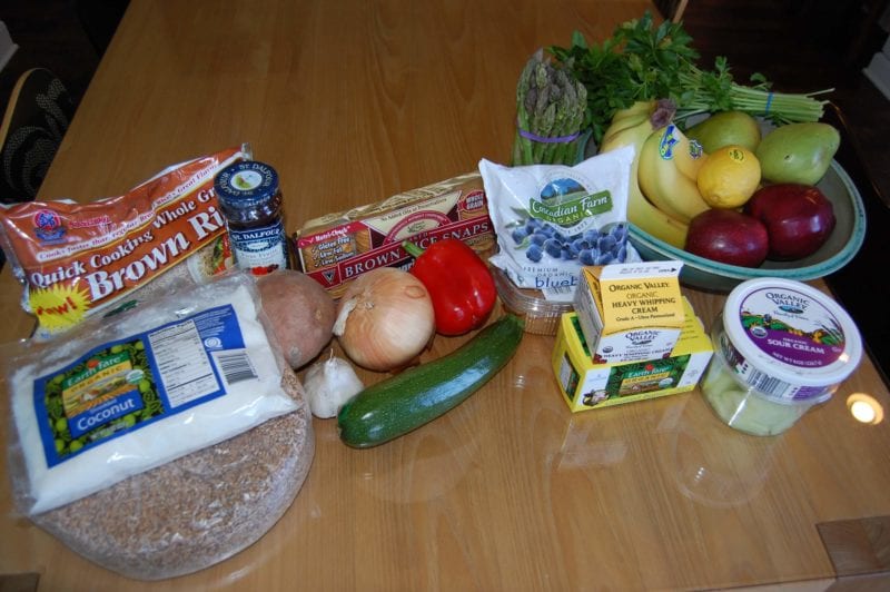 Groceries from Earth Fare that include fresh produce, frozen blueberries, brown rice, shredded coconut, sour cream, and heavy cream. 