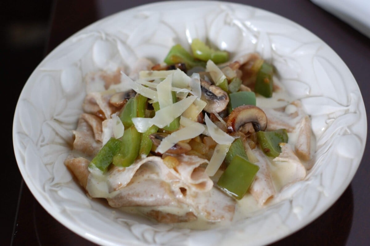 Bowl of homemade Alfredo pasta topped with mushrooms, peppers, and cheese.