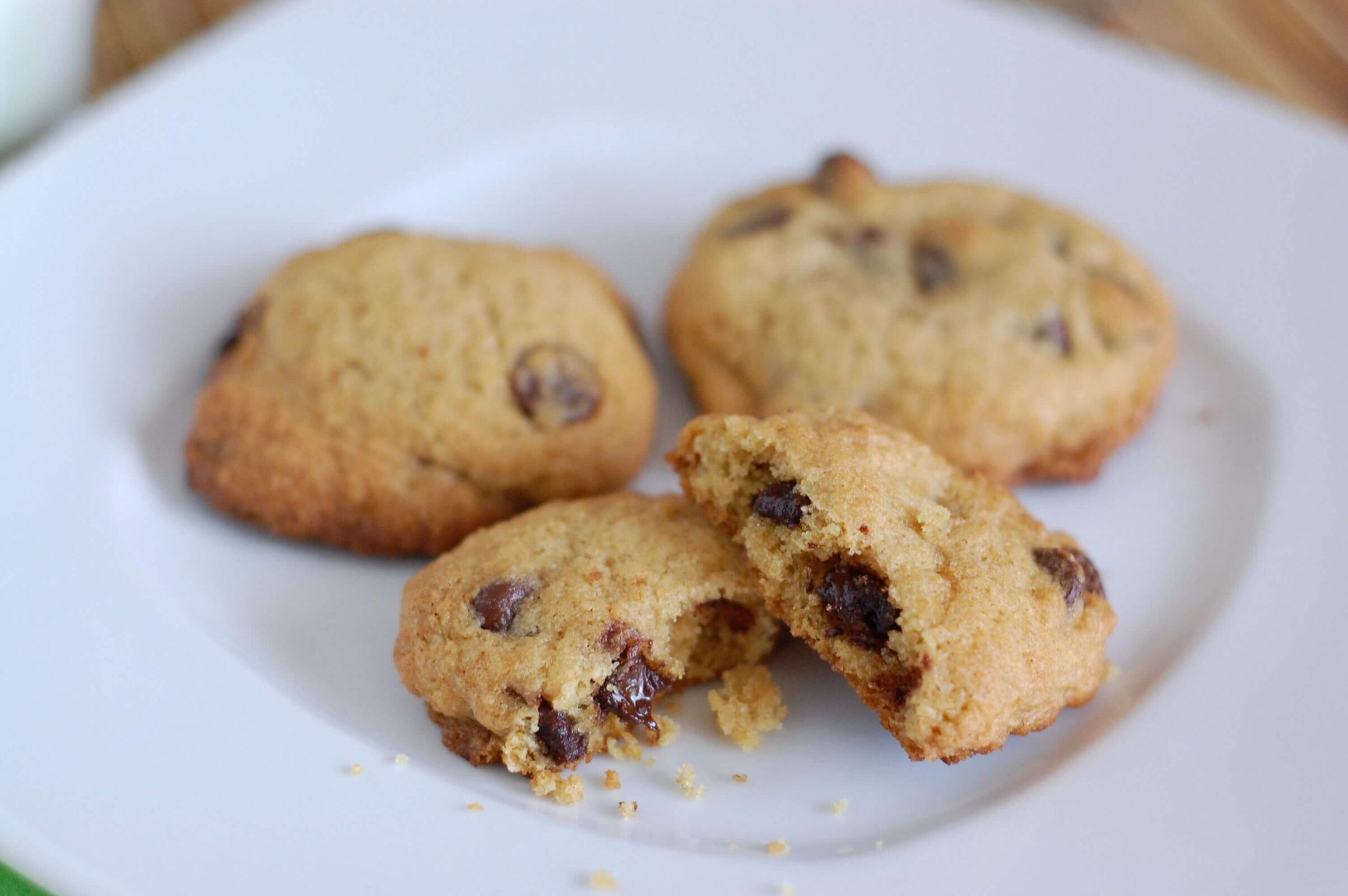 Three fresh baked chocolate chip cookies on a white plate. 