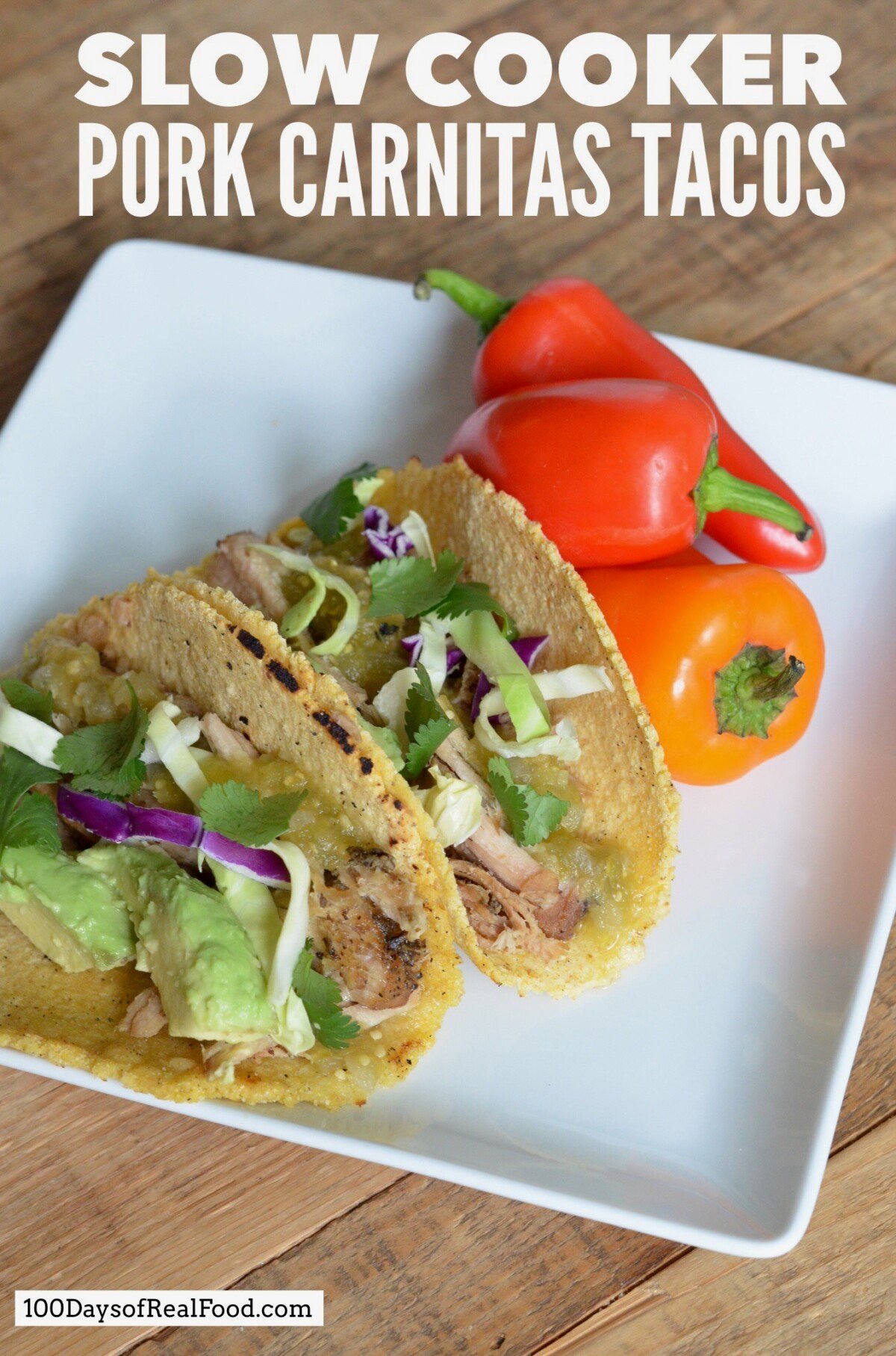 Two pork carnitas tacos in corn tortillas topped with avocado and cilantro with three red and orange peppers on the side. 