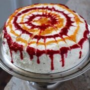 Round cake with white frosting and tie dye berry sauce