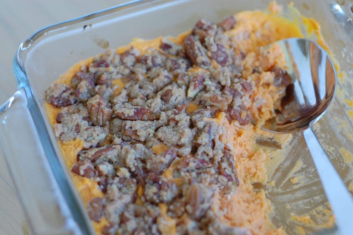 Clear casserole dish with homemade sweet potato casserole topped with crunchy pecan topping.