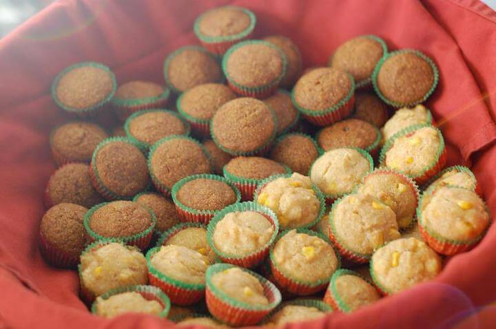 Pumpkin bread muffins and corn bread muffins in a large basket with a red cloth towel. 