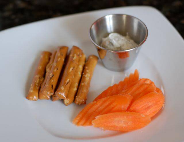 Pretzel sticks and carrot slices with a side of ranch dip on a plate.
