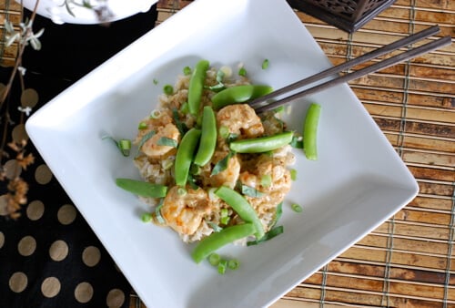 Green Curry Shrimp with sugar snaps and green onions on top of a white dinner plate.