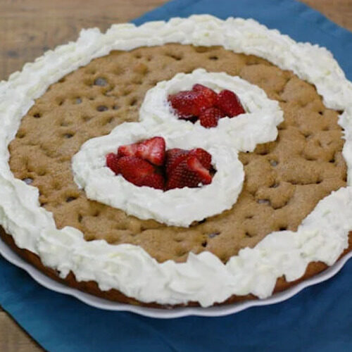 A homemade cookie cake with whipped cream number 8 in the middle filled with strawberries.