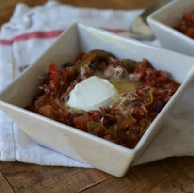 Slow Cooker Red and Green Chili in a white bowl topped with sour cream and cheese