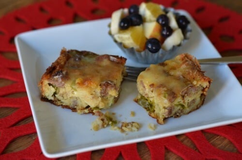 Two small pieces of a homemade holiday breakfast casserole with a side of fruit. 