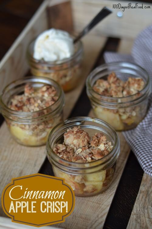 Four small mason jars filled with warm cinnamon apple crisp with one topped with vanilla ice cream.