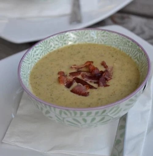 A large bowl of homemade broccoli cheese soup in a decorative bowl topped with bacon