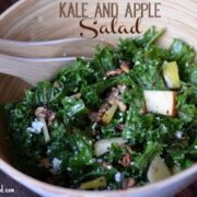kale and apple salad topped with nuts in a wooden bowl.