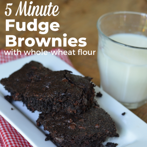 Three homemade brownies stacked on a white dish with a glass of cold milk.
