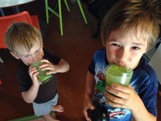 Two young boys enjoying their green smoothies in a cup.