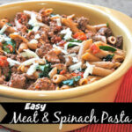 Meat and spinach pasta topped with shredded cheese in a dish.