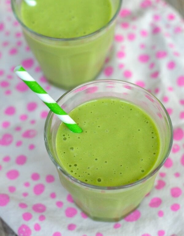 Two green smoothies in clear drinking glasses with a green and white striped straw.