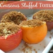 four tomoatos in a baking dish filled with couscous and topped with breadcrumbs.