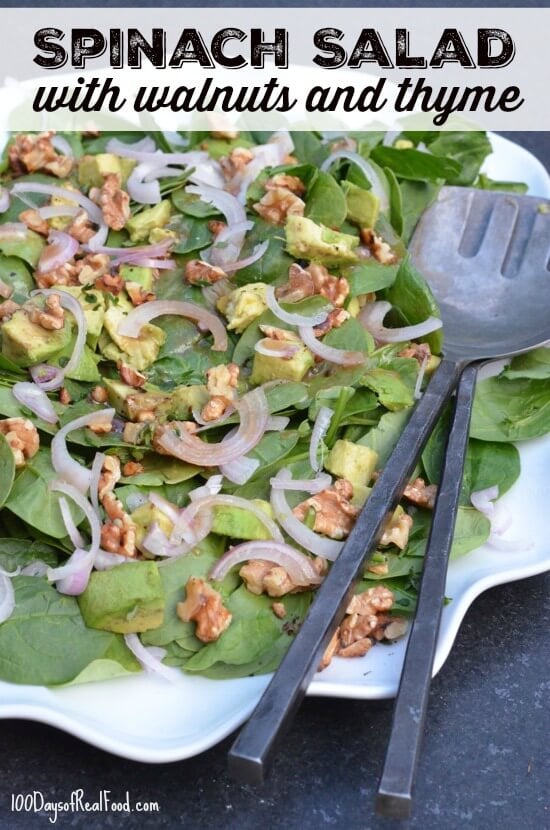 Plate of spinach leaves, chopped onions, avocado, and walnuts.