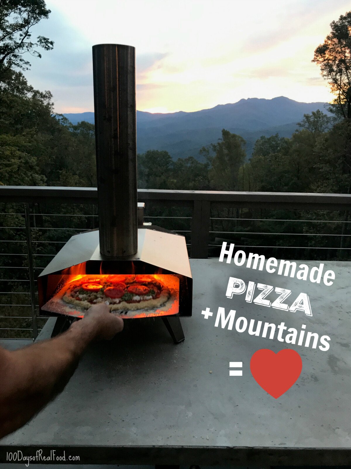 Homemade pizza being placed inside a portable oven overlooking the mountains at a tiny home. 