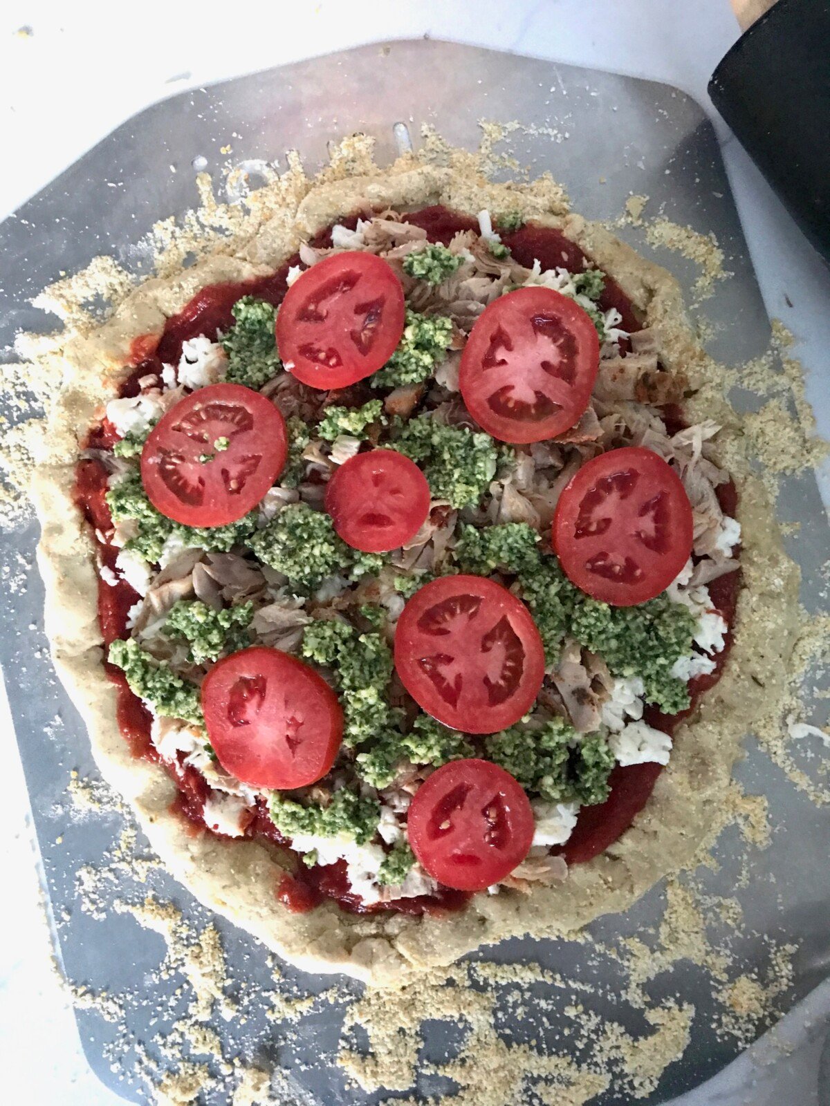 Homemade Chicken Pesto Pizza on a pizza tray before going in the oven.