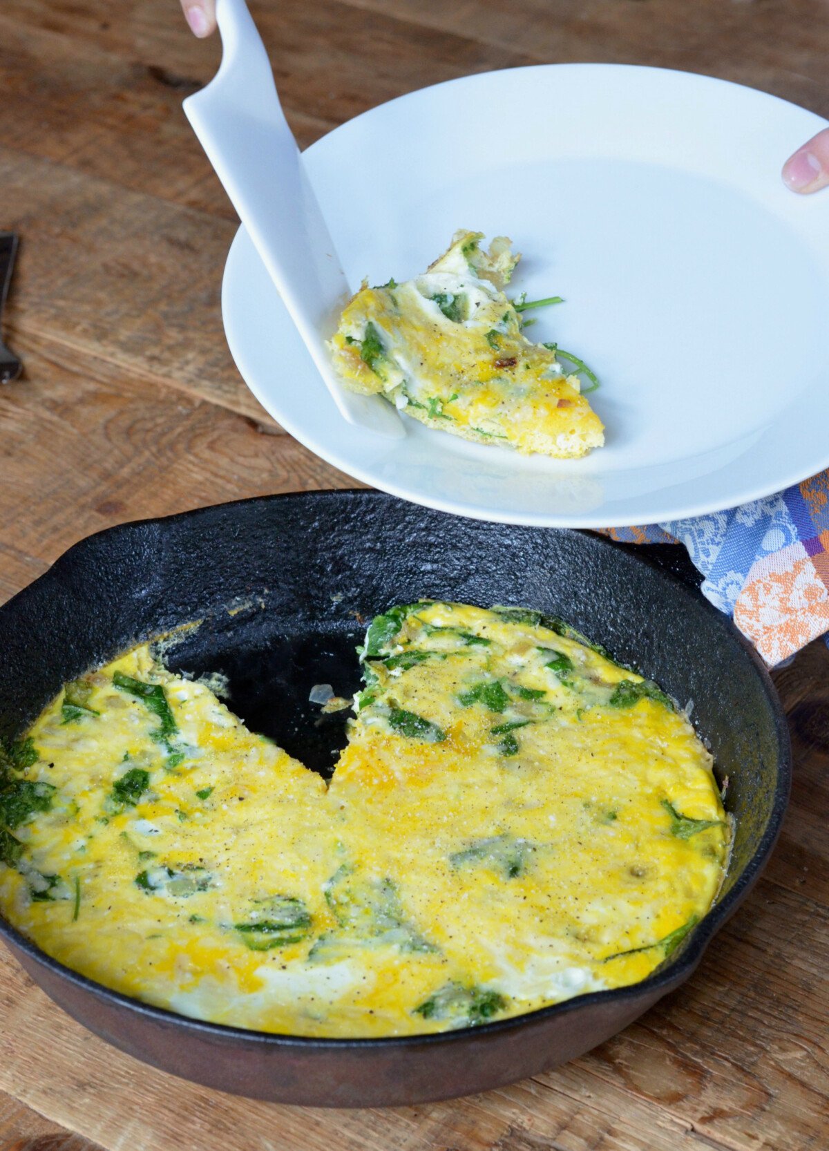 Kale and Egg Frittata in a cast iron pan while someone takes a piece and puts it on a white plate