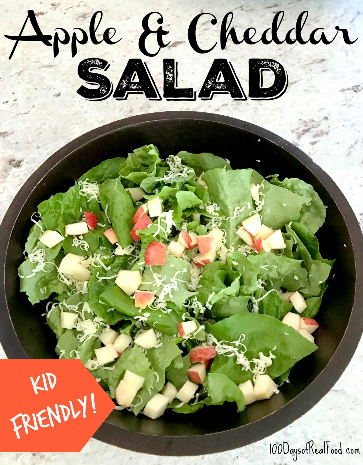 Large black salad bowl filled with leafy greens, apple pieces, and shredded cheddar.