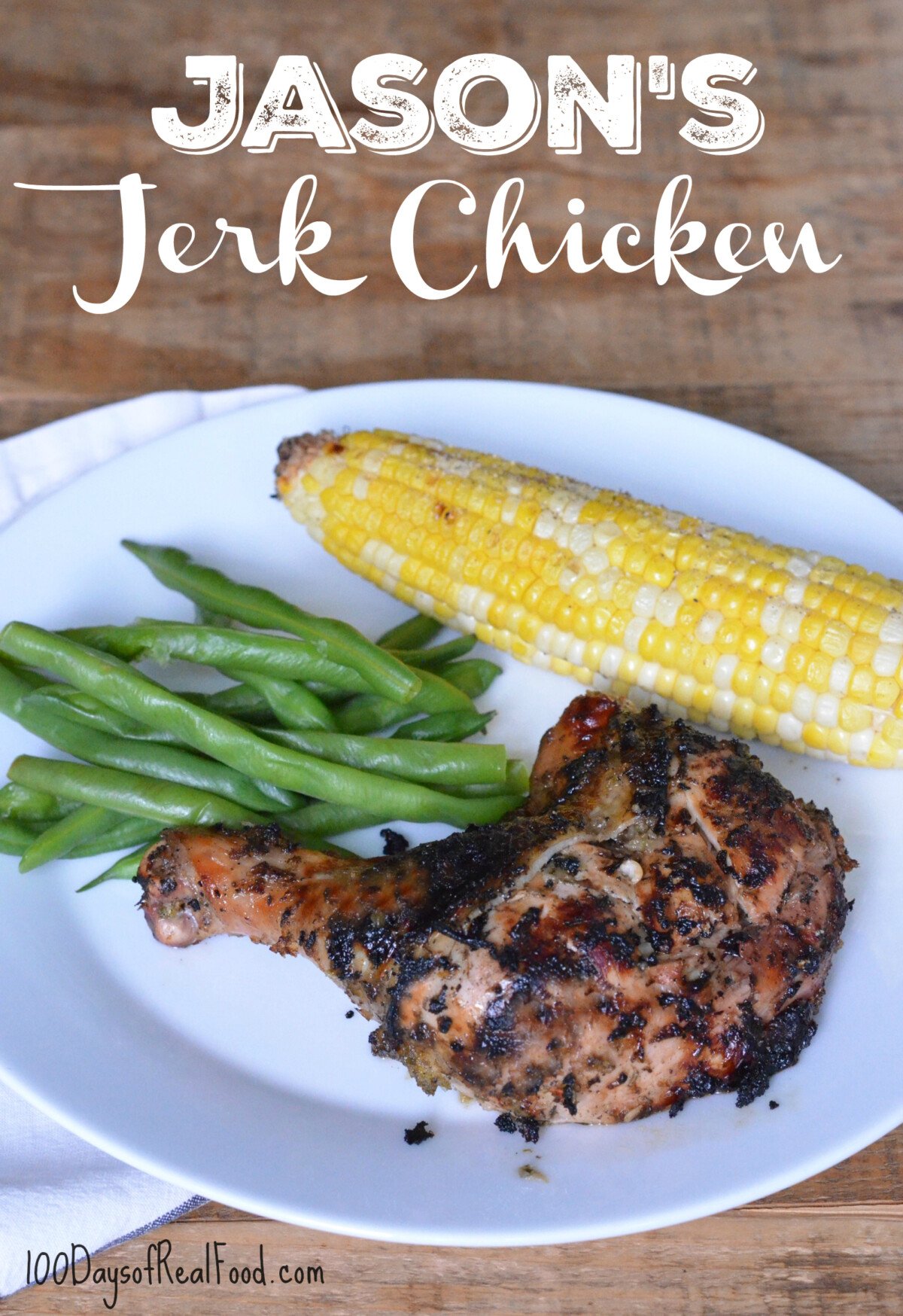 A white dinner plate with grilled jerk chicken leg, green beans, and an ear of corn. 