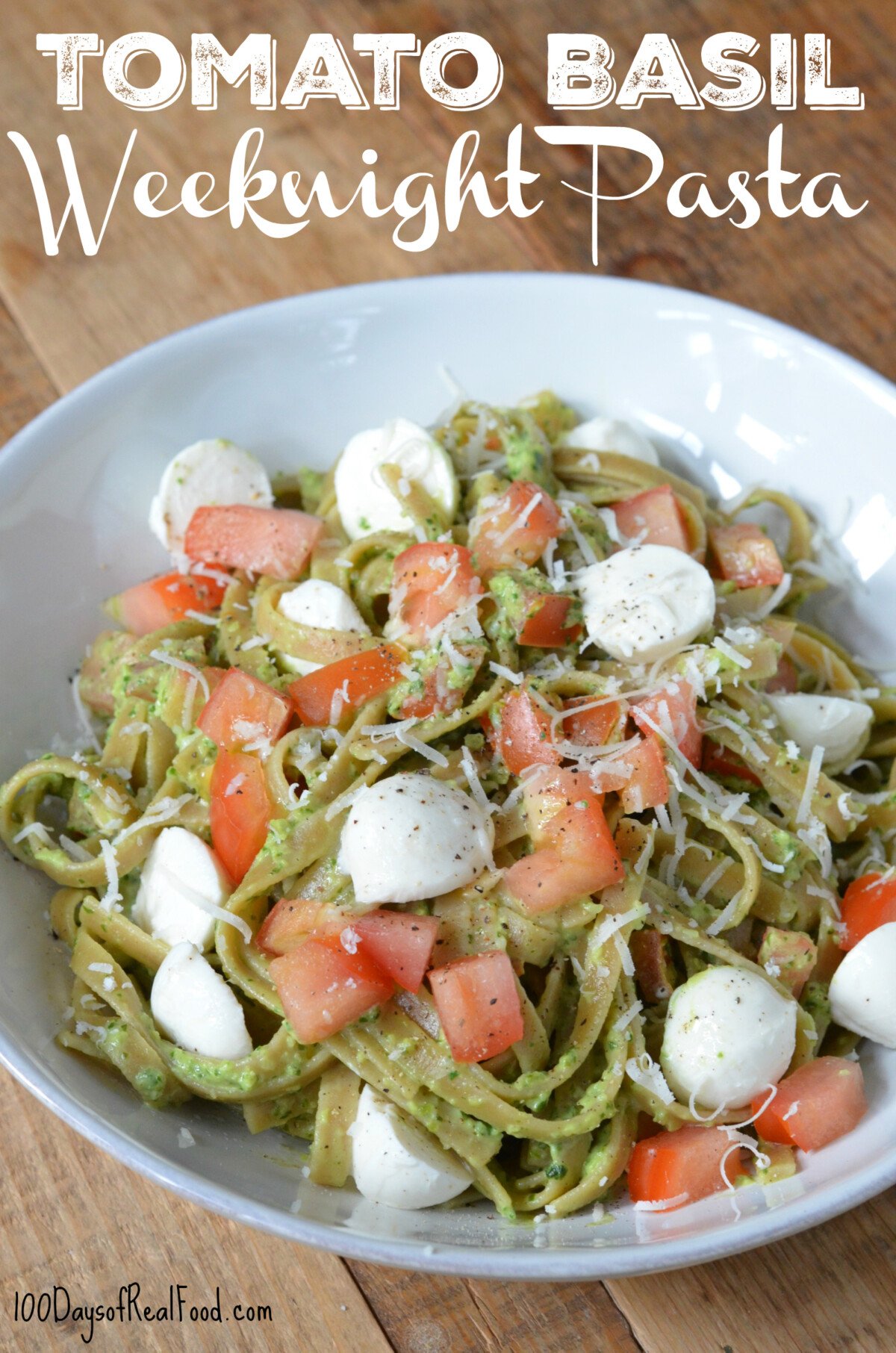 Pasta with tomatoes, pesto, mozzarella pieces, and topped with more shredded cheese in a bowl.