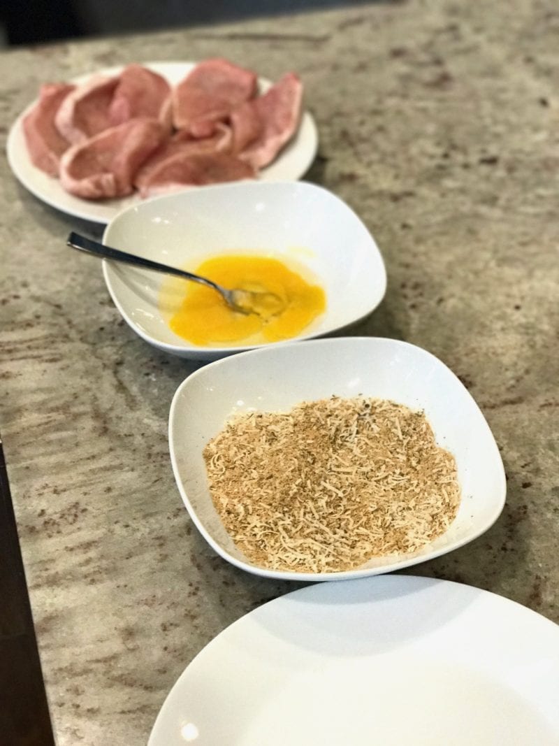 Weeknight Pork Milanese on 100 Days of Real Food - assembly line of dishes with raw pork, beaten eggs, bread crumb mixture, and empty plate 