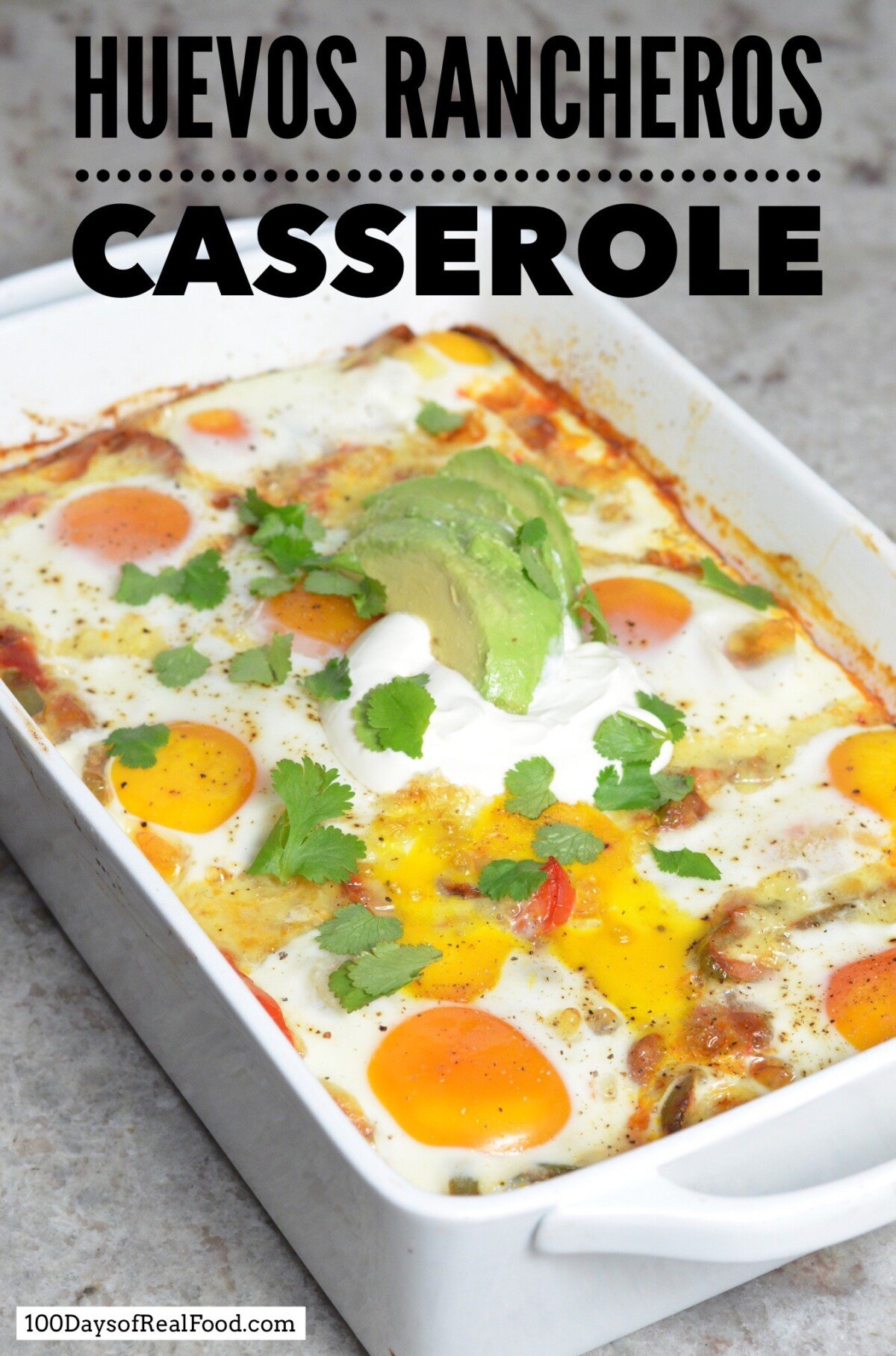 Large white baking dish with cooked Huevos Rancheros Casserole topped with sour cream, avocado slices, and cilantro.