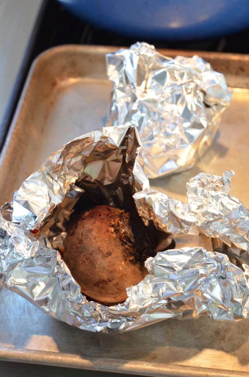 Baking beets wrapped in tinfoil on a baking sheet