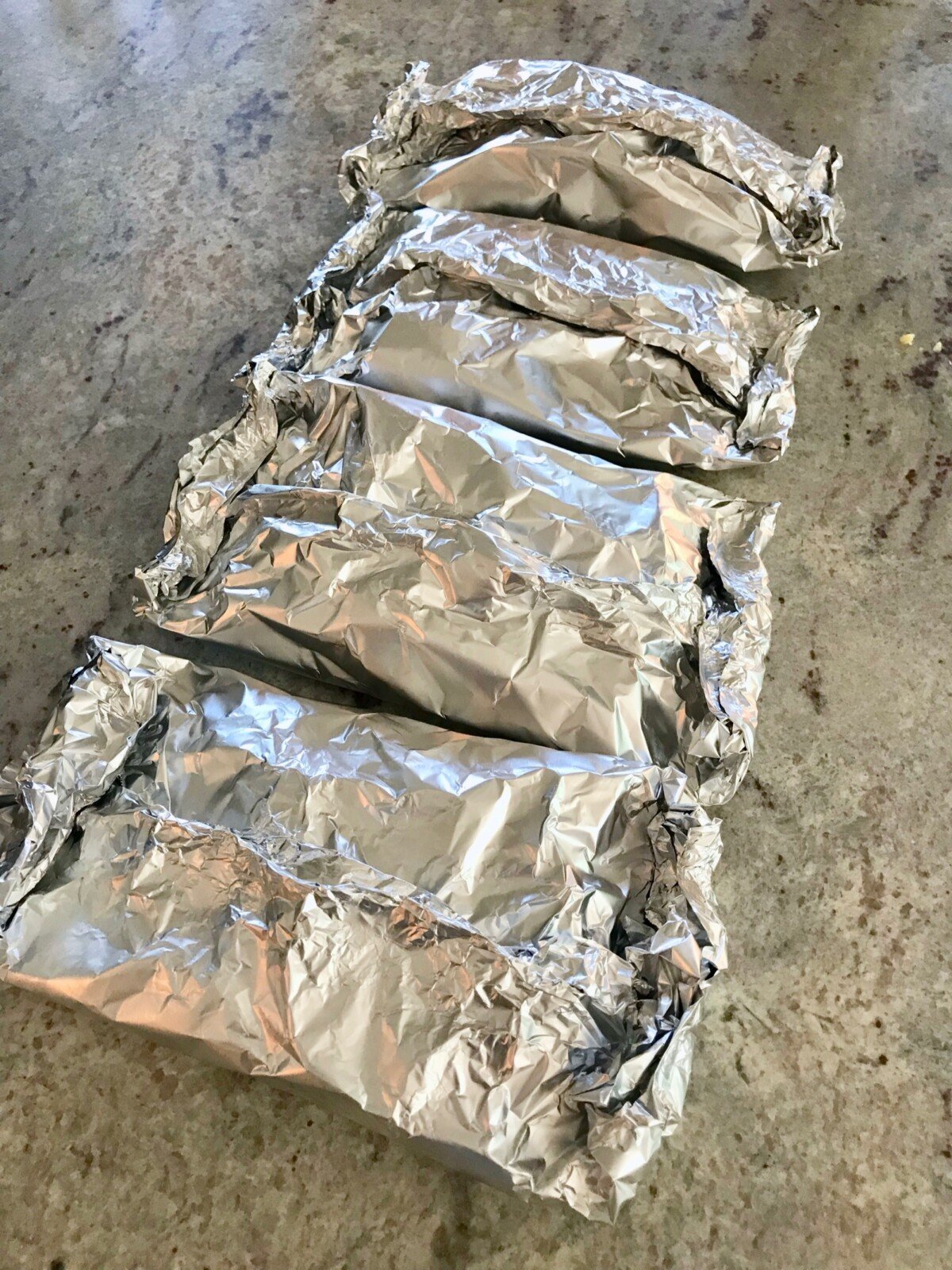 Four chicken fajita foil packets in aluminum foil sitting on a counter preparing to cook on a campfire.