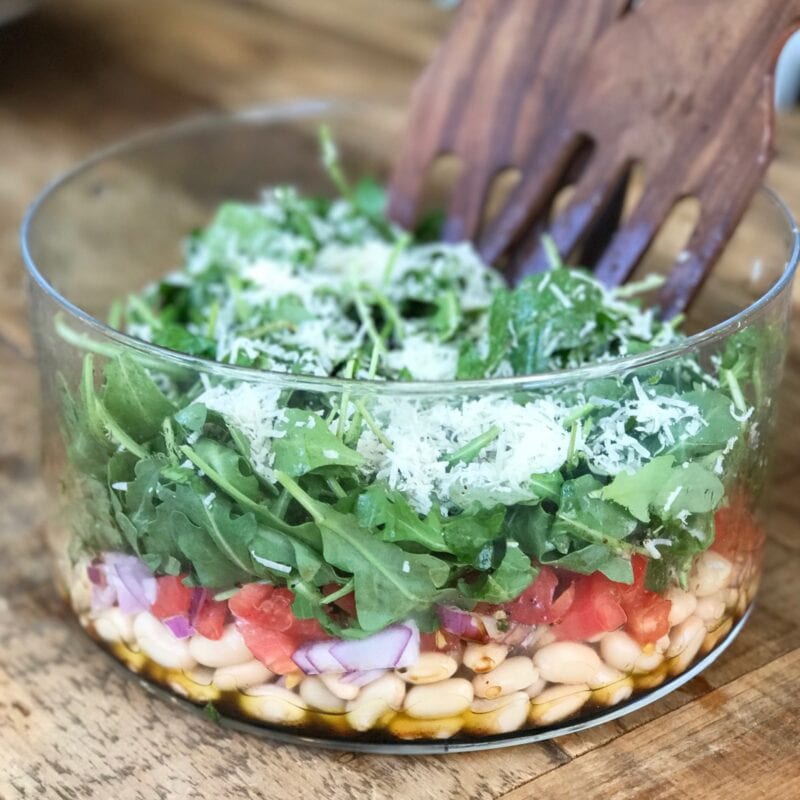 White bean salad in a glass bowl with serving spoons