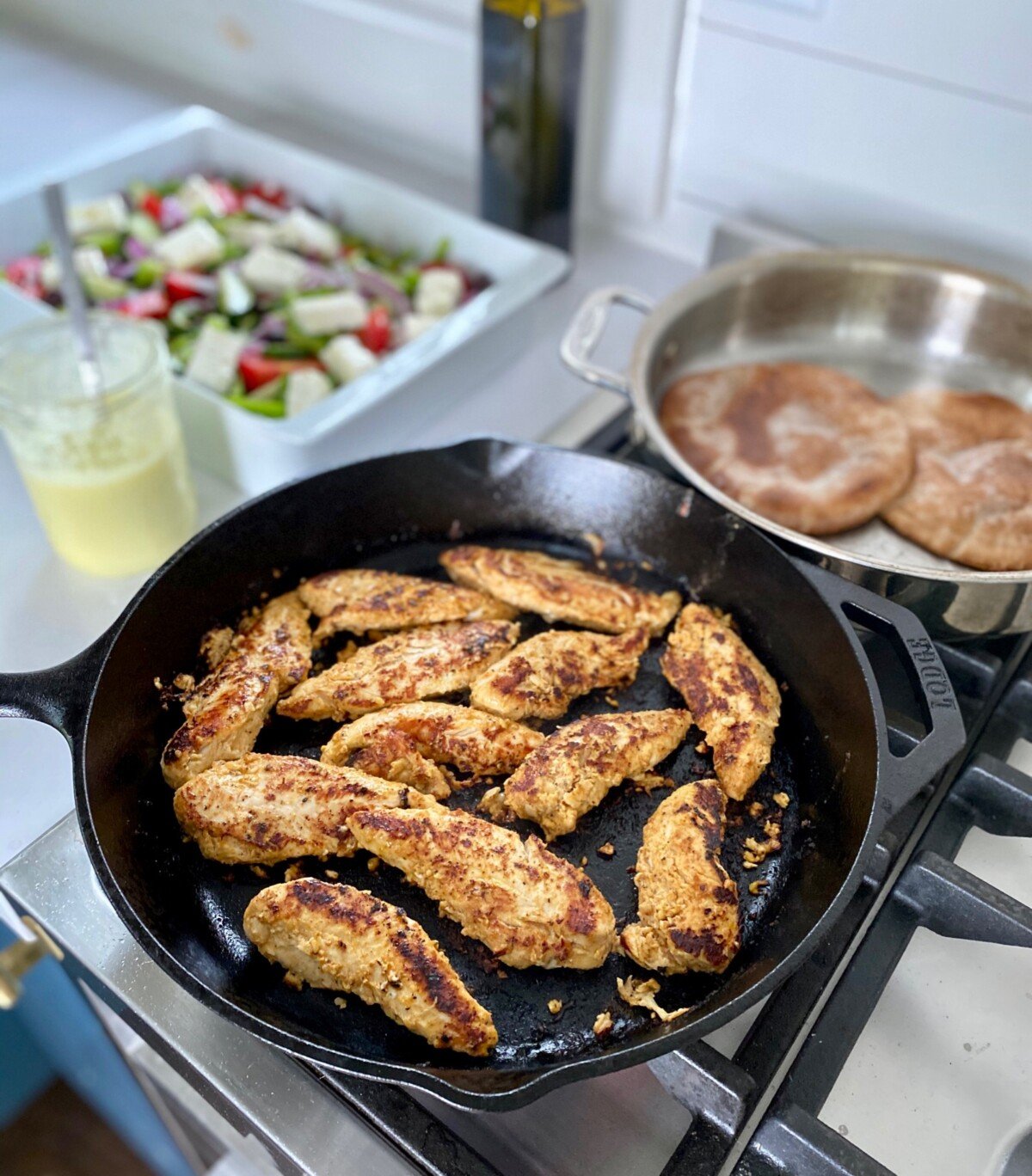 Chicken Shawarma cooking in a skillet on the stove with pitas being warmed up next to them.