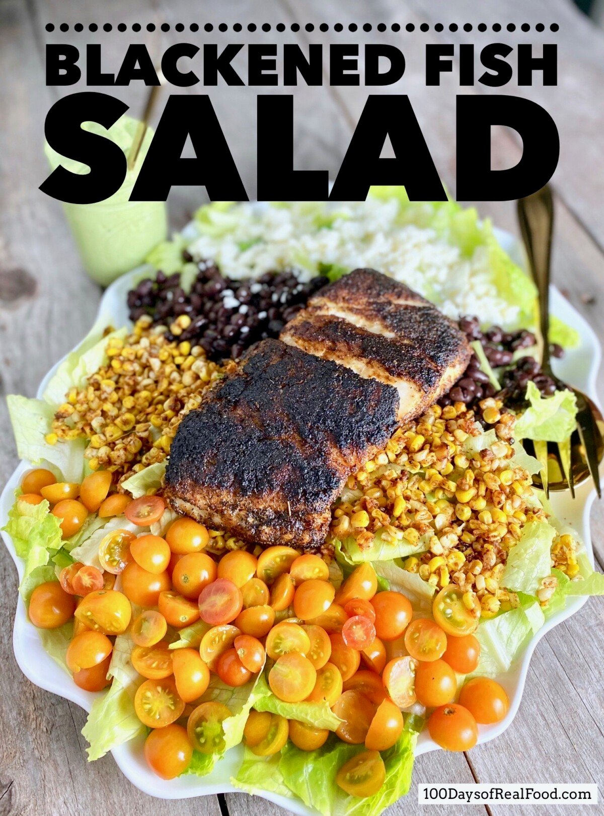 Large serving plate piled with lettuce, tomatoes, corn, black beans, cheese and topped with a large piece of blackened fish.