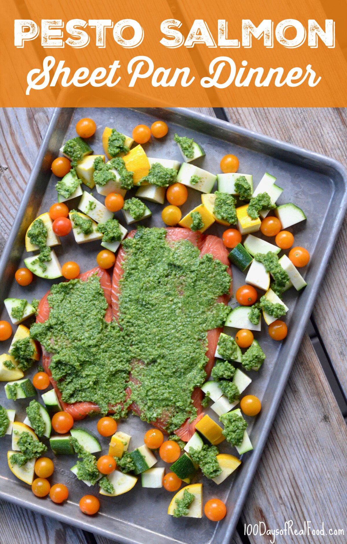 Two pieces of salmon, cherry tomatoes, and cut up pieces of squash topped with pesto on a baking sheet before going into the oven.