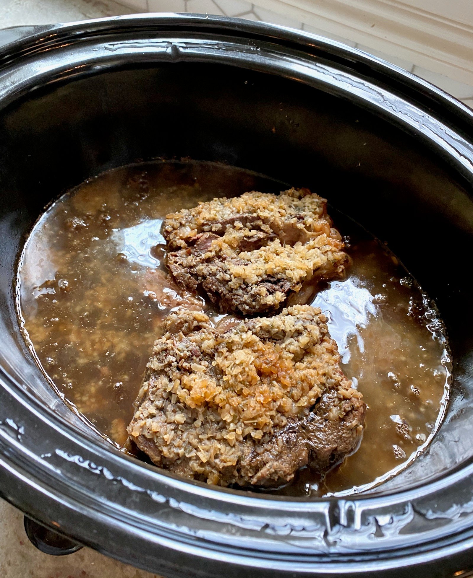 Chuck roast with ingredients for French Dip in a slow cooker.