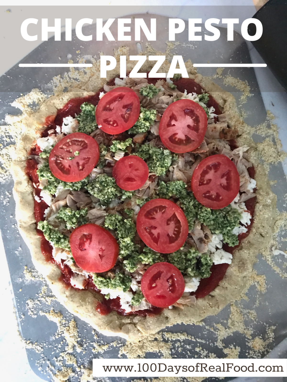 A homemade pizza with chicken, pizza sauce, pesto, and tomatoes, about to go into the oven. 