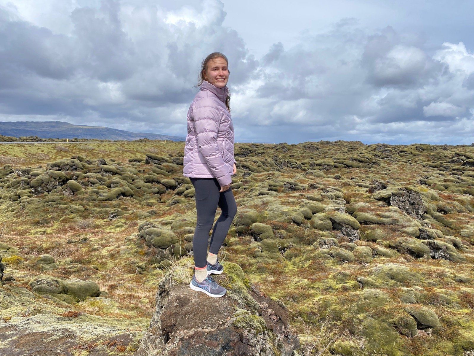 Teen girl standing on moss covered mounds in Iceland.
