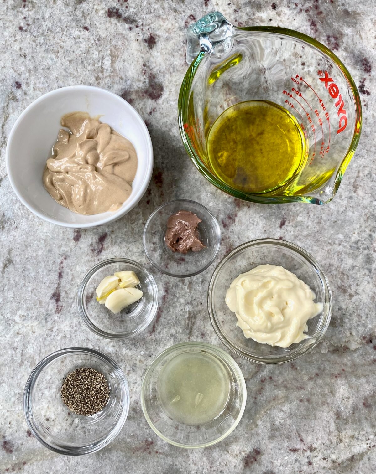 Ingredients in clear bowls to make homemade Caesar salad dressing.