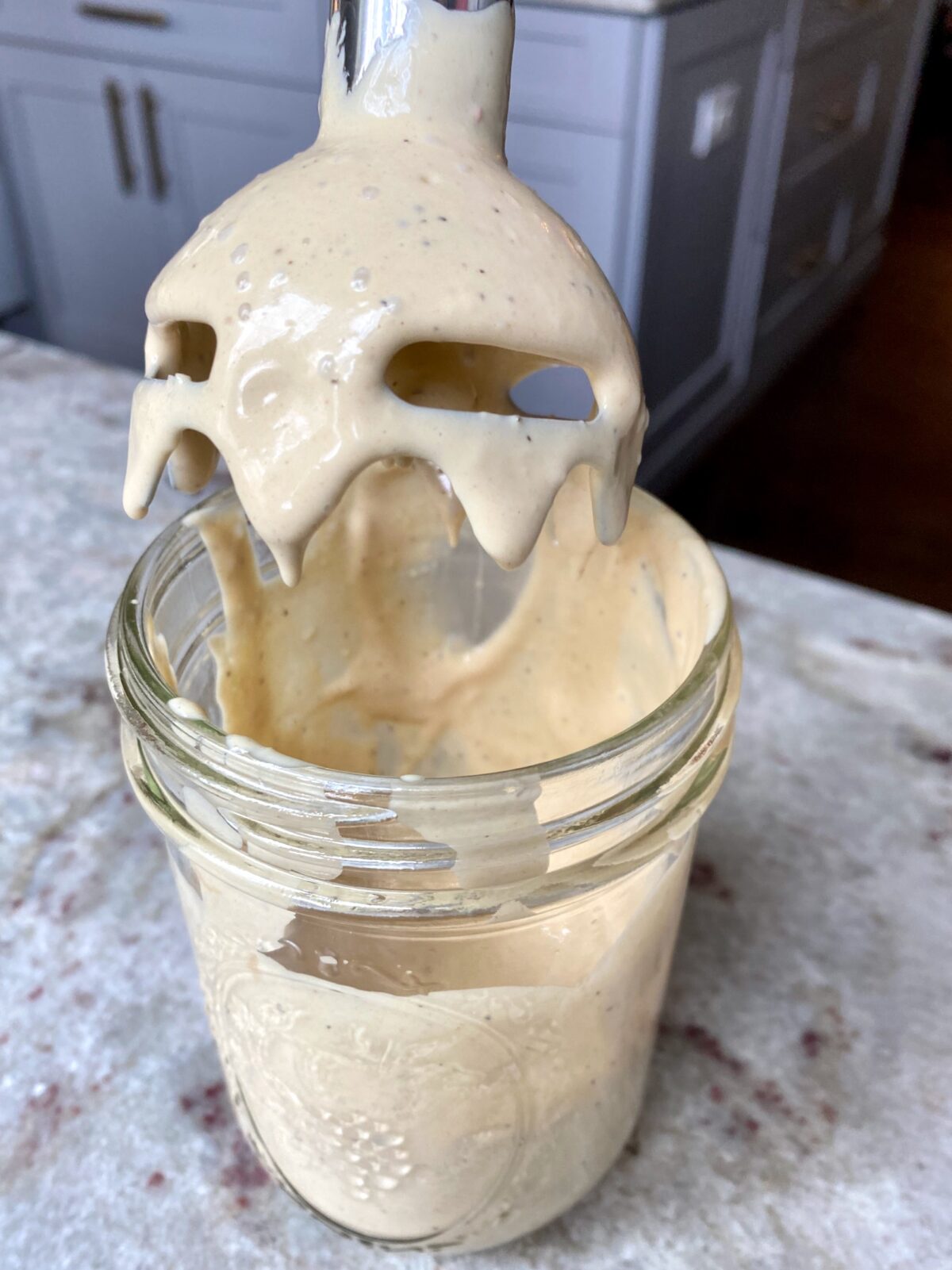 Mason jar with ingredients blended together using a hand mixer for Caesar salad dressing.